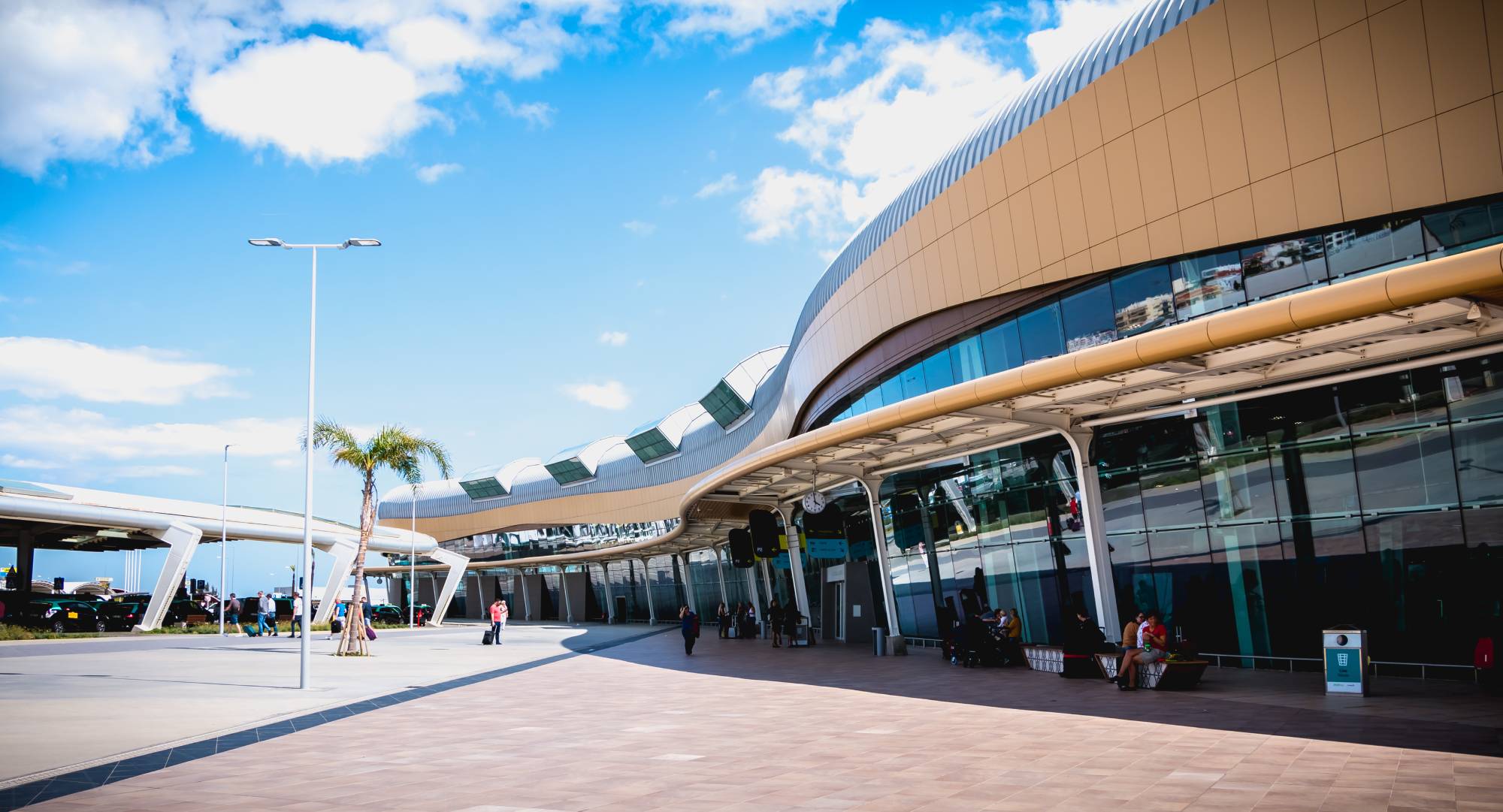Modern airport terminal with a clear blue sky and palm trees.