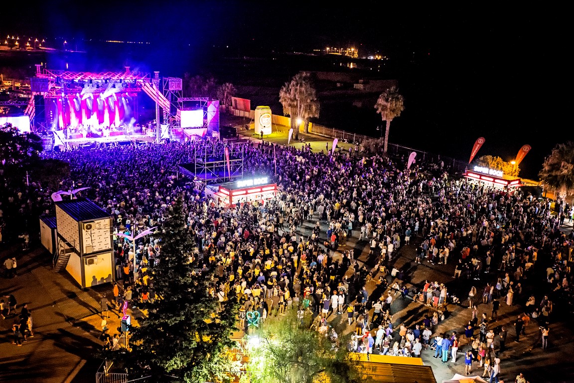 Large crowd enjoying a nighttime outdoor concert by the water.